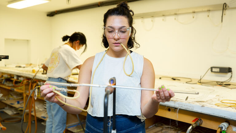 A student in protective eyewear working on a neon piece