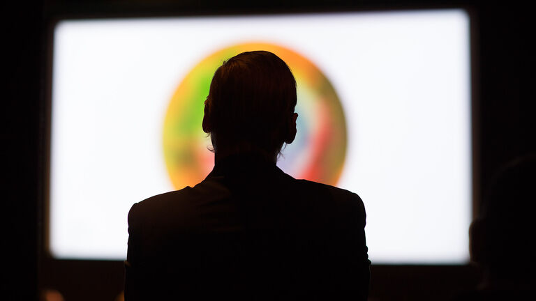 A silhouette of a person in front of a large screen.