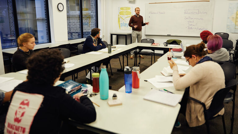 A professor lecturing to a small group of students in a classroom. 