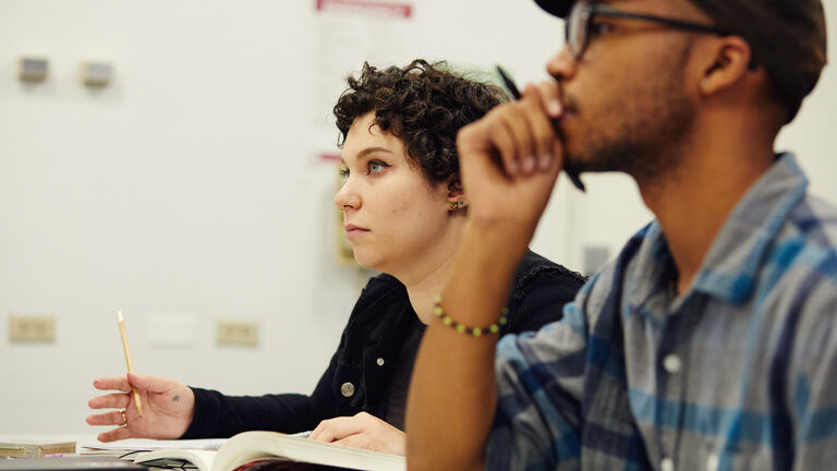 Two people sitting in a classroom facing forward. 