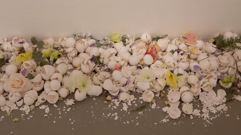 Egg shells and plastic flowers spread out on the ground. 