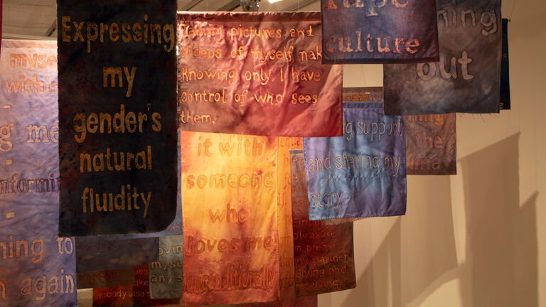 Various, colorful fabric pieces hanging from the ceiling of a gallery space. 