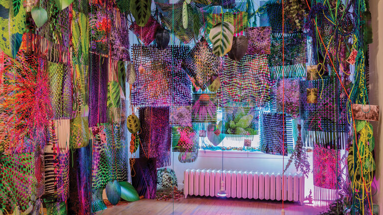 Various colorful prints, leaves and lights hanging from the ceiling of a gallery space.