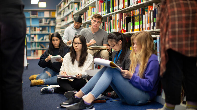 Students sitting against bookshelves