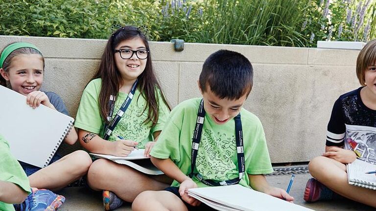 A group of kids sitting outside with sketchbooks. 