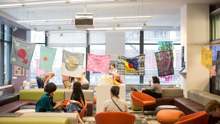 A group of students sit below fabric art in a campus space