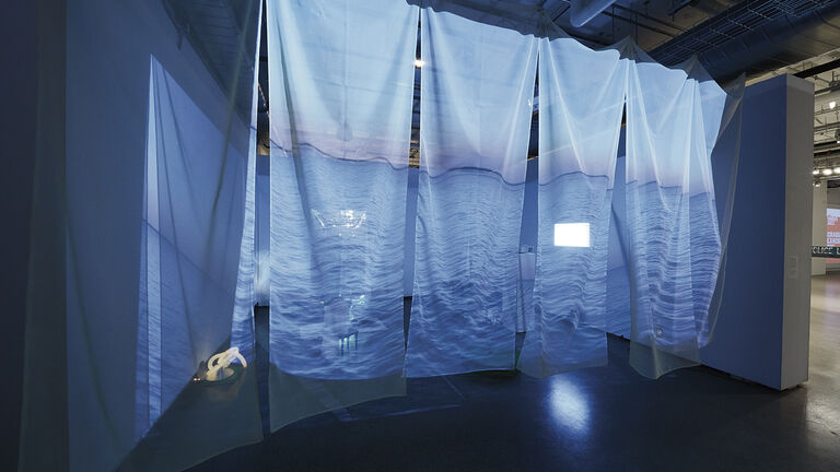 Multiple large, transparent sheets with a projection of water hanging in a gallery space.