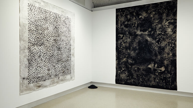 Two large black and white canvases hanging up in a gallery. 