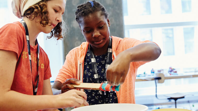 Two students wrap colored cloth around a rod