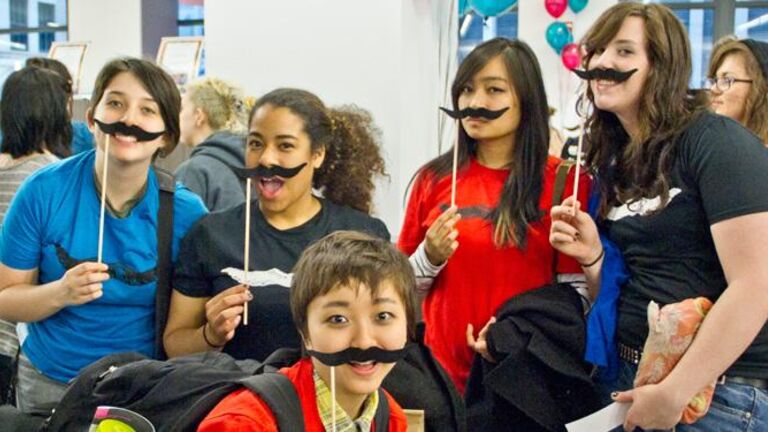 Five students holding construction paper mustaches. 