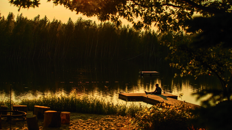 A person sits on a dock overlooking a lake with a sepia filter.