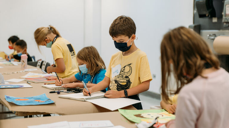 Children wearing masks drawing in a classroom.