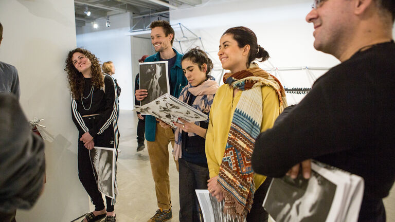 A group of students holding prints talk amongst themselves