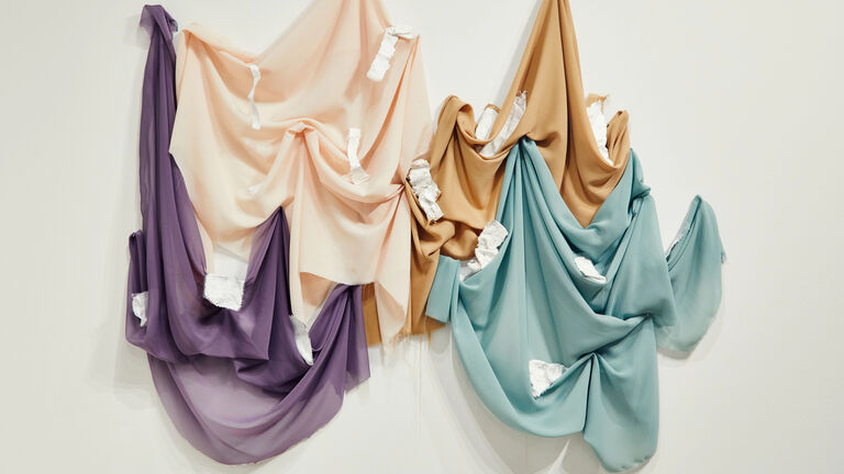 Purple, cream, orange and blue hanging fabrics on a gallery wall. 