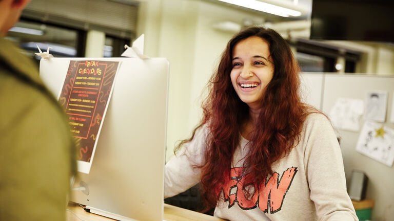 A student sits behind a computer and smiles.