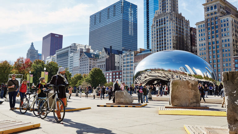 Skyscrapers in the background with the Chicago CloudGate “Bean” surrounded by people.