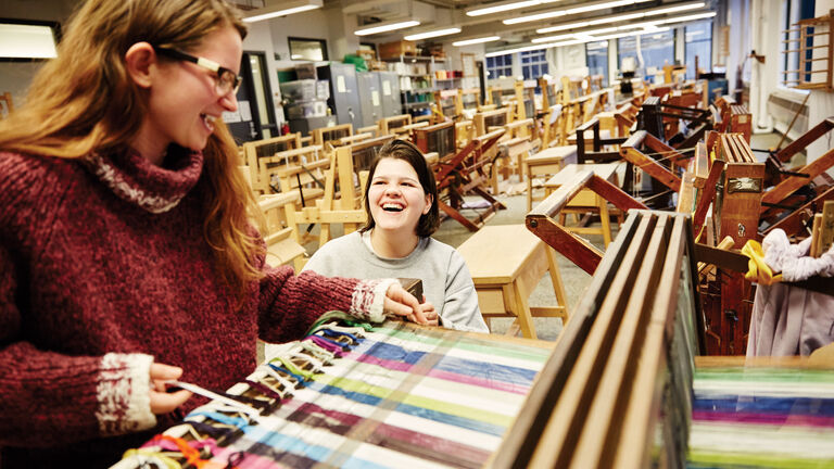 Two students work on a large loom in a classroom.