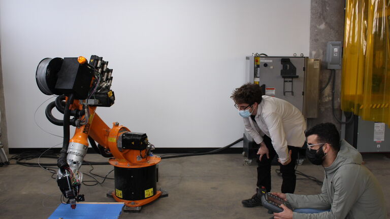 A student and faculty member using a Kuka robot to make a piece