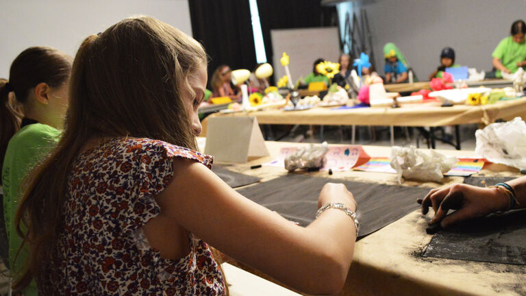 A young student working at a large table in a classroom. 