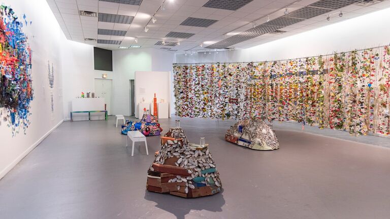 A modern art gallery with sculptures on the concrete floor and colorful hangings on the walls