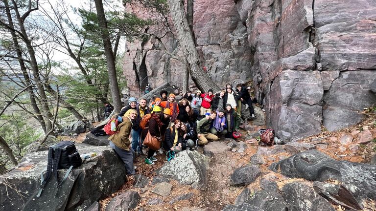 A group of students pose on the side of a mountain in climbing gear