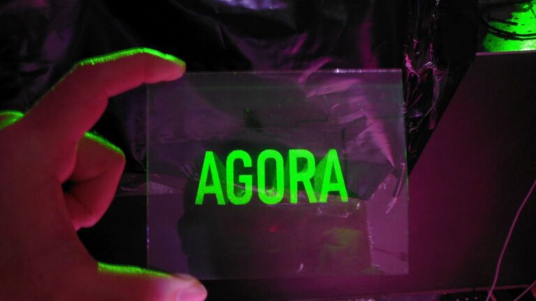 a hand holds a plate with the word AGORA printed on it in bright green letters