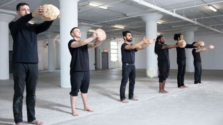 Performers hold large rocks in a gallery space.