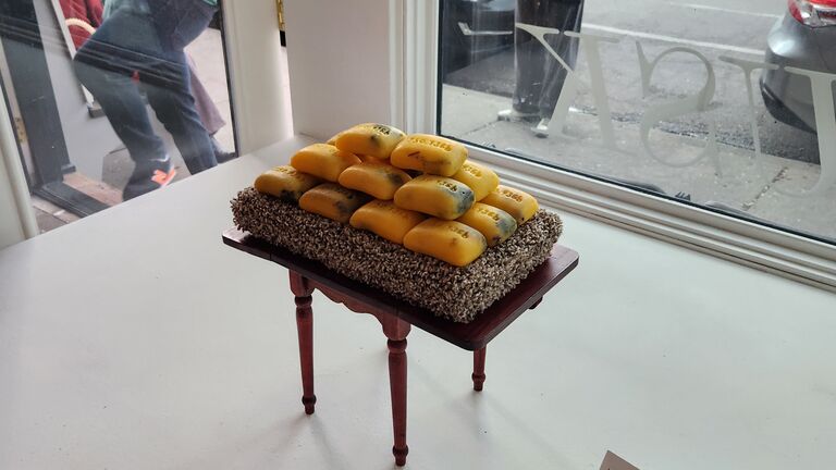 A sculpture made up of soaps sits atop a tiny table in a gallery window