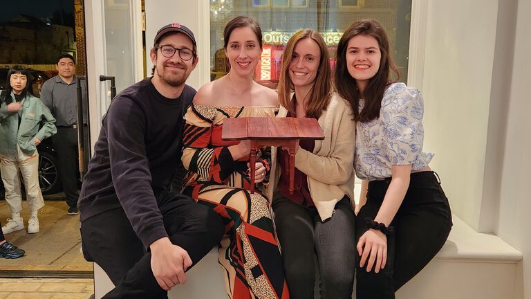 Four artists hold a tiny table in a gallery space