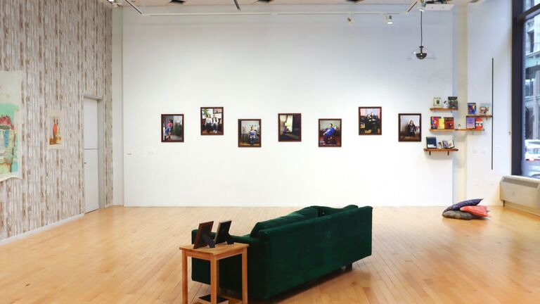 installation shot of exhibition including a green couch in the center of the room with artwork installed on the walls