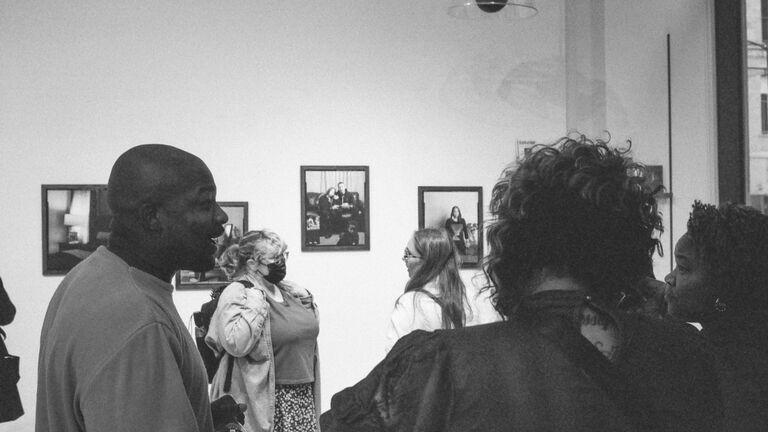 Artist in the foreground talking with visitors at the exhibition opening