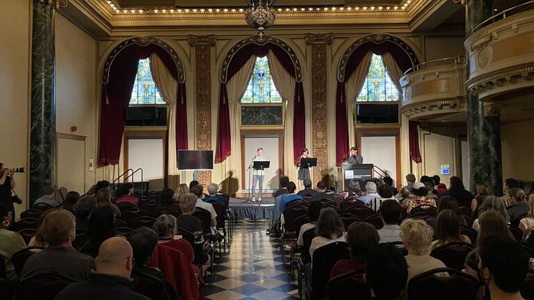 An image of three people on stage at the SAIC ballroom reading into microphones.