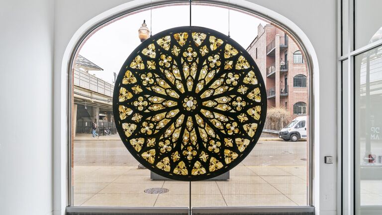 circular stained glass window that is black and green in front of a larger street-facing window in a white room