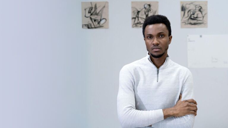 Painter Luke Agada standing in front of three of his figurative abstract paintings on a white background