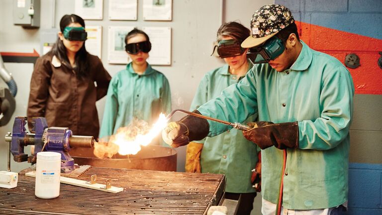 Four students wearing safety equipment and welding metal