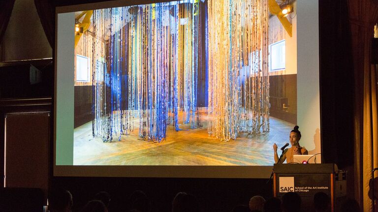 An image of artist Wu Tsang at a podium in front of a screen