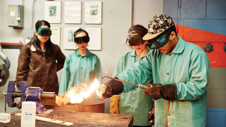 Four students wearing safety equipment and welding metal