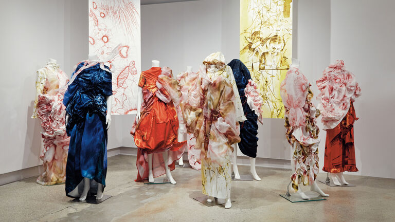 Seven mannequins wearing colorful garments against a white backdrop