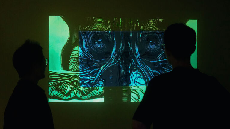 Two people watch a bright blue and green projection