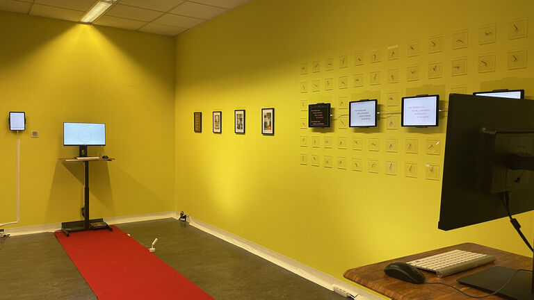 A series of framed art and screens hanging in a row on a yellow wall