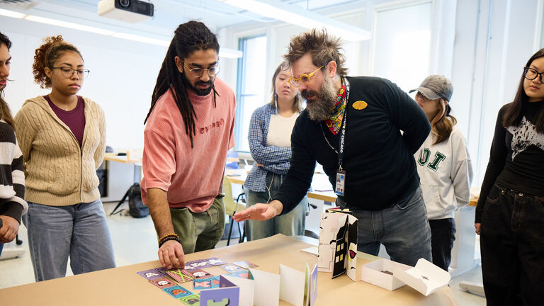 A group of SAIC students gather around a professor at a table.