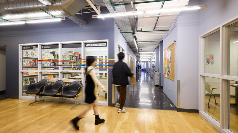 Two students walk past a classroom and down a hallway.