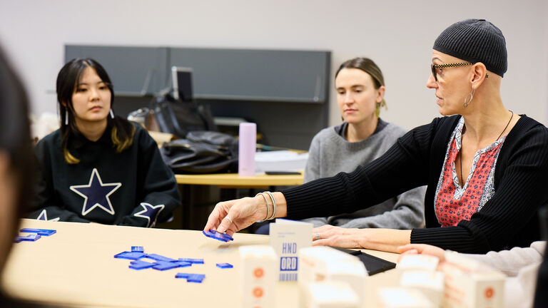 Two SAIC students and a faculty member sit at a table in a classroom.