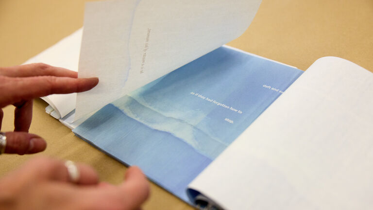 A person flipping the page in a book, landing on a blue page that says "as if they had forgotten how to stop".