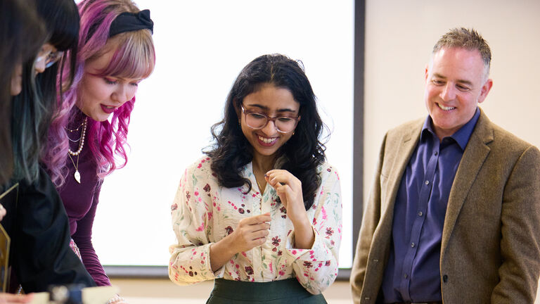 Three SAIC students and a faculty member gather around a table.