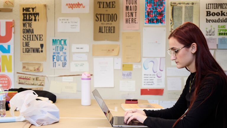 A student sits at a desk looking at their laptop.