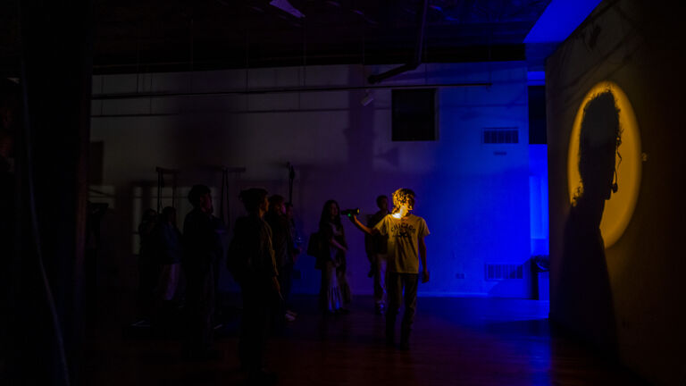 Picture of a performance happening in a space, with reflections of red and orange shadows and lights.