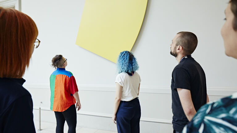 A group of five adults with varying skin tones, ages, and gender identities, viewing an art installation. 