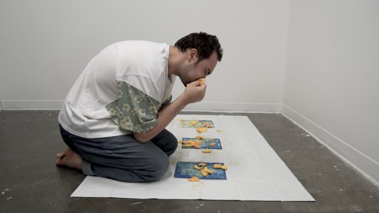 Evan performing by eating oranges over cyanotypes. The cyanotypes have antiquated language about queer folks on them. 