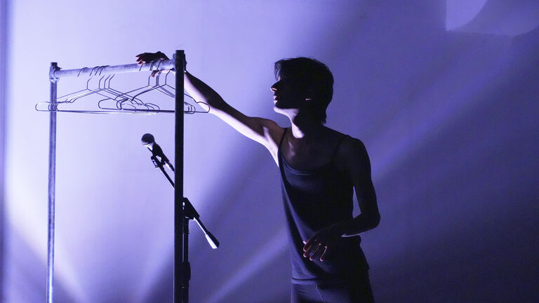 Hesam reaching for empty hangers, while a brillant lavender light ripples in the background.